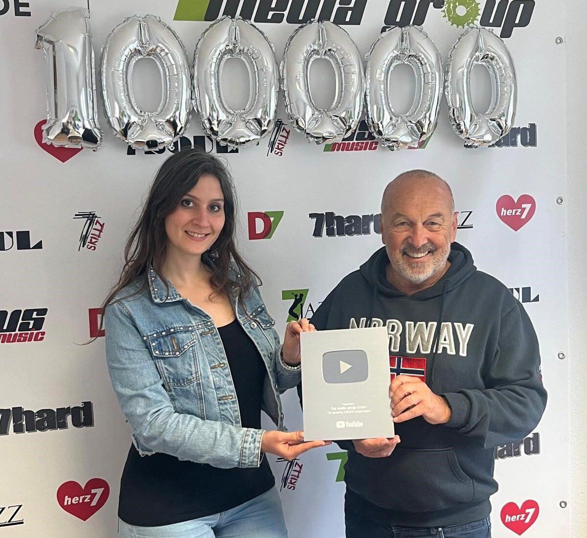 COO Natalie Lemberger und CEO Hans Derer mit dem YouTube-Creator-Award in Silber vor der 7us-Fotowand mit 100.000-Ballons
